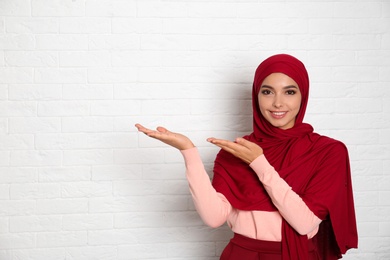 Photo of Portrait of young Muslim woman in hijab against brick wall. Space for text