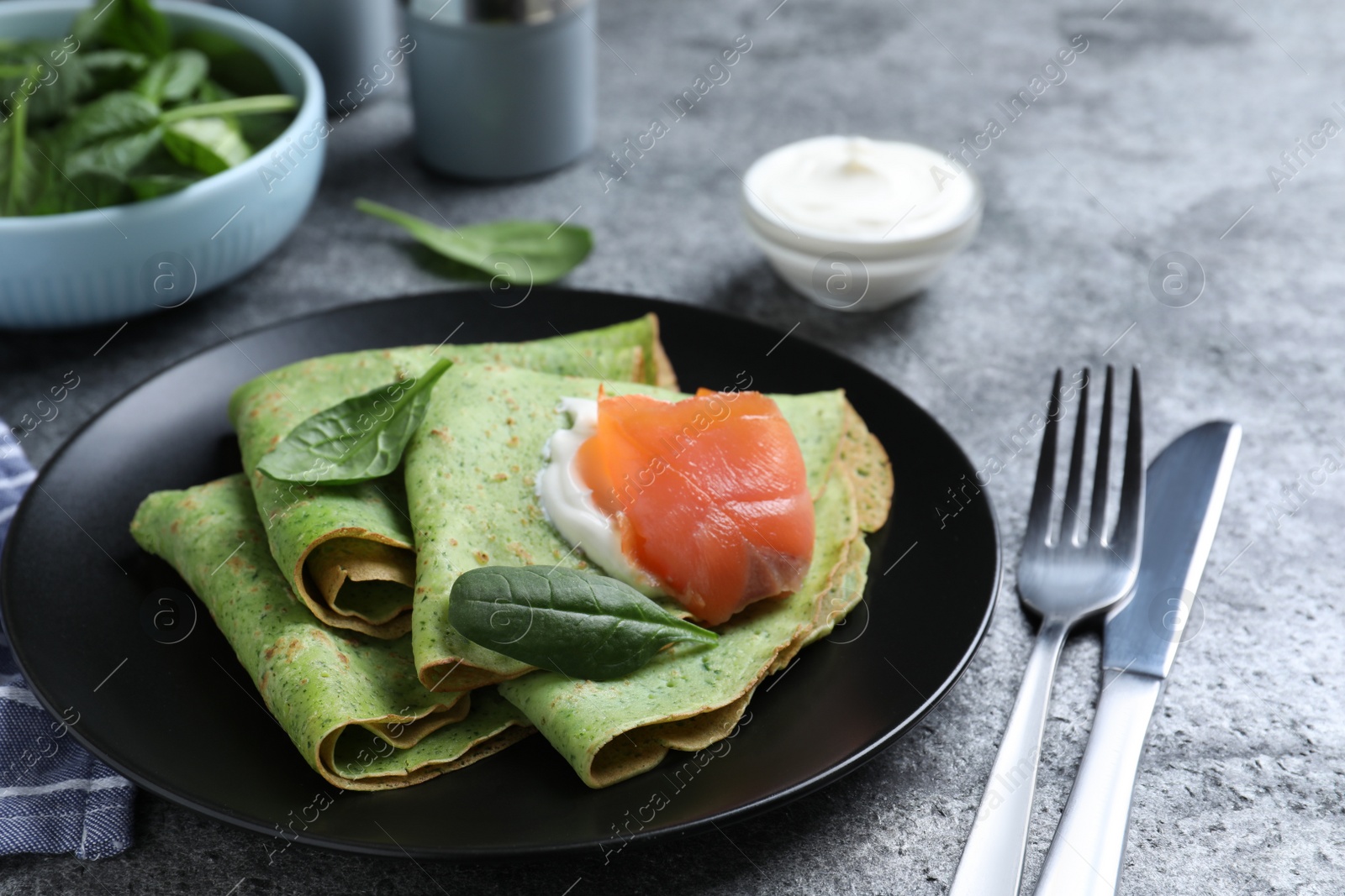 Photo of Delicious spinach crepes with salmon and cream served on grey table