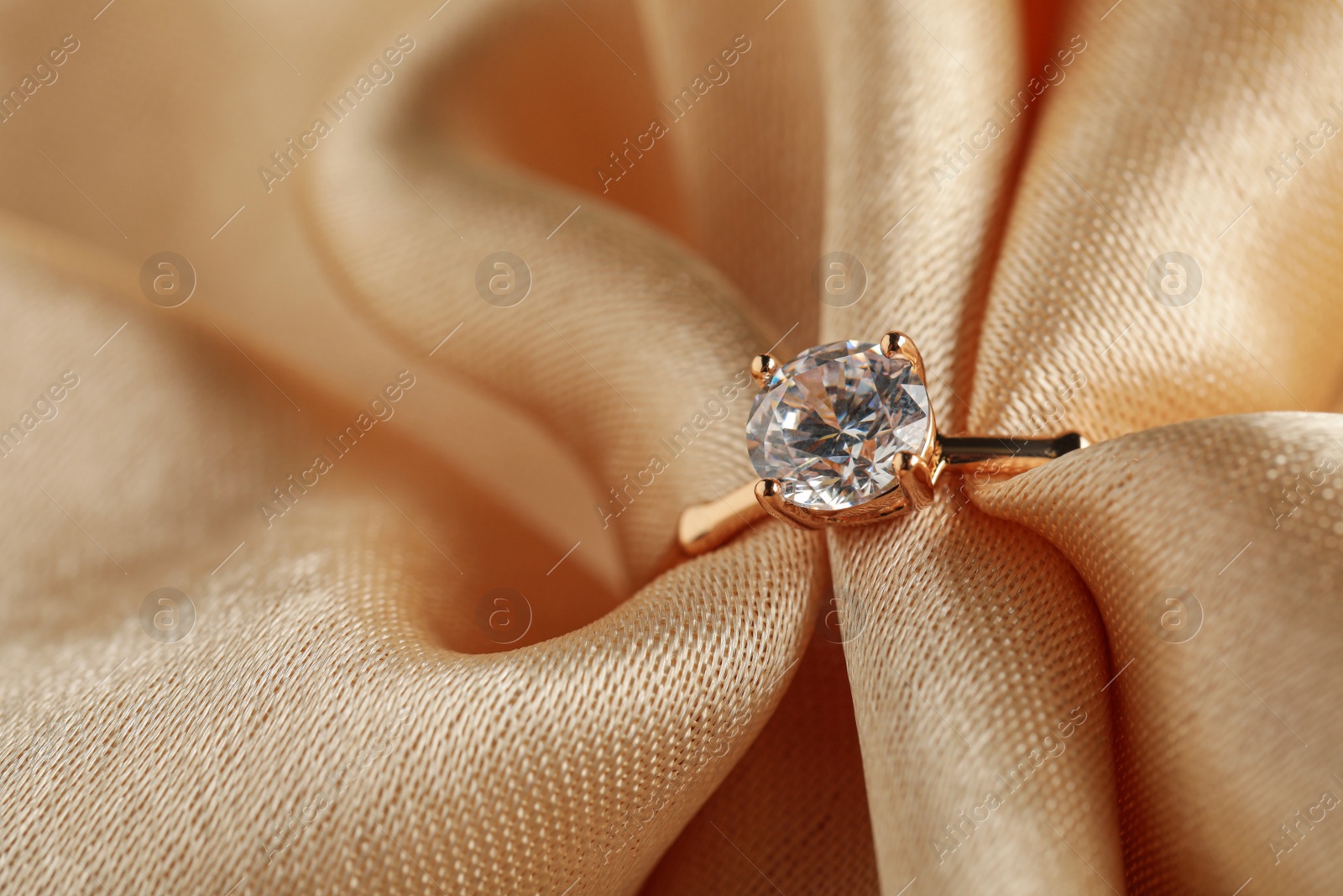 Photo of Beautiful engagement ring with gemstone on beige fabric, closeup