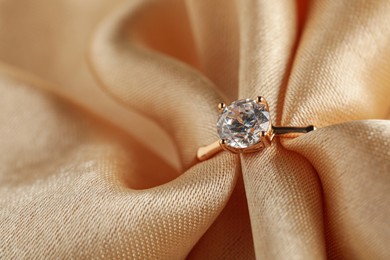 Photo of Beautiful engagement ring with gemstone on beige fabric, closeup
