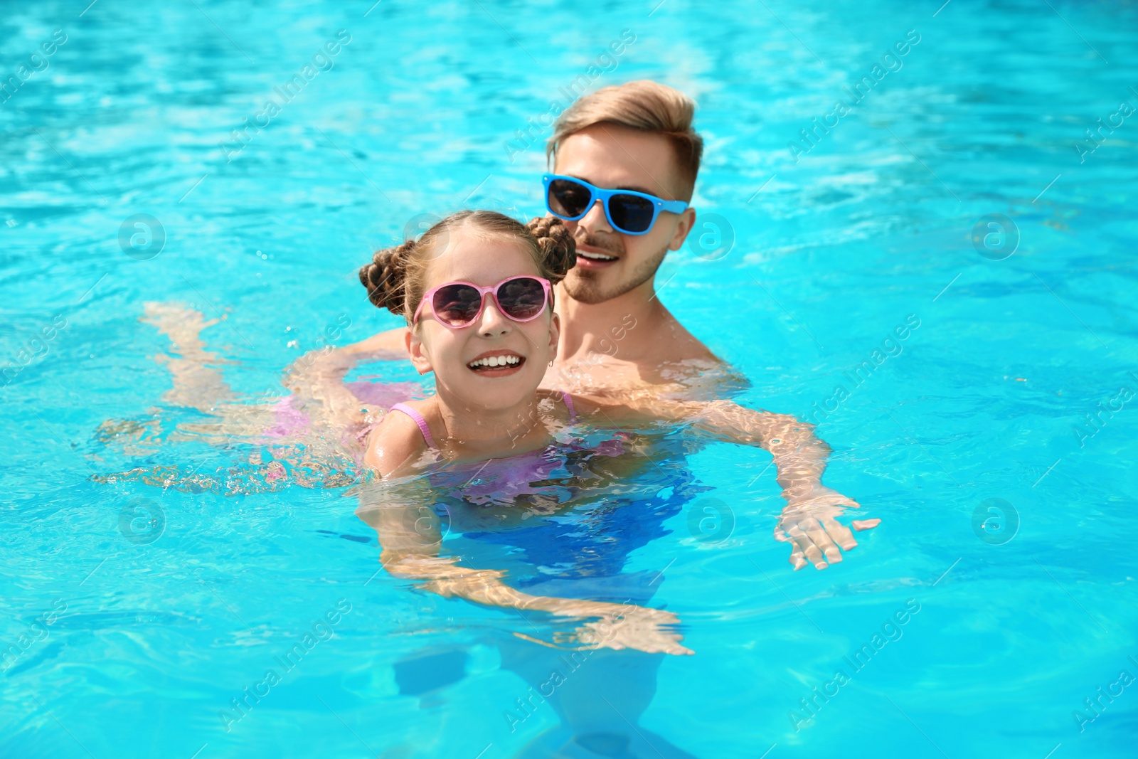 Photo of Young man teaching his daughter to swim in pool