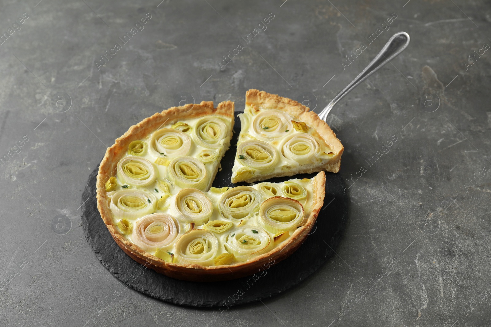 Photo of Tasty leek pie with cake server on dark textured table