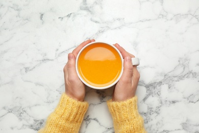 Photo of Woman holding cup with sea buckthorn tea at white marble table, top view