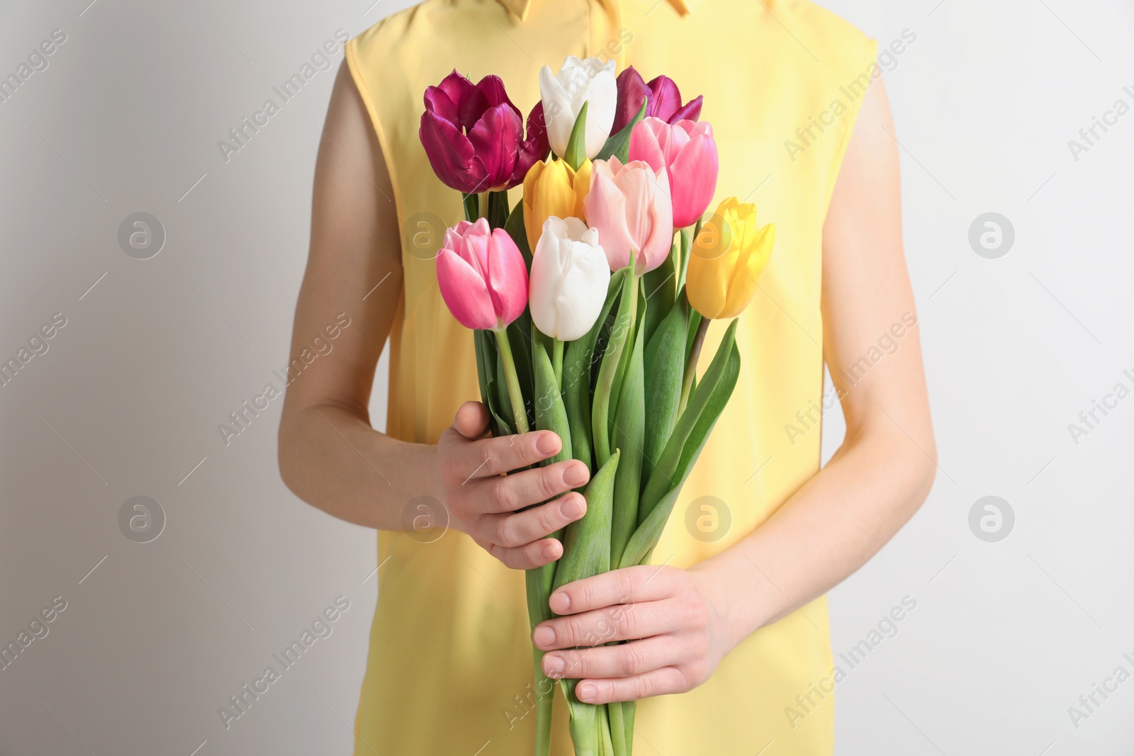 Photo of Girl holding bouquet of beautiful spring tulips on light background, closeup. International Women's Day