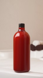 Photo of Red bottle of bubble bath and towels on tub indoors