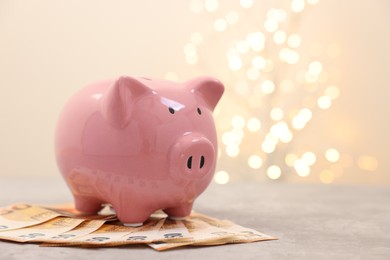 Photo of Piggy bank with euro banknotes on grey table against blurred lights, space for text