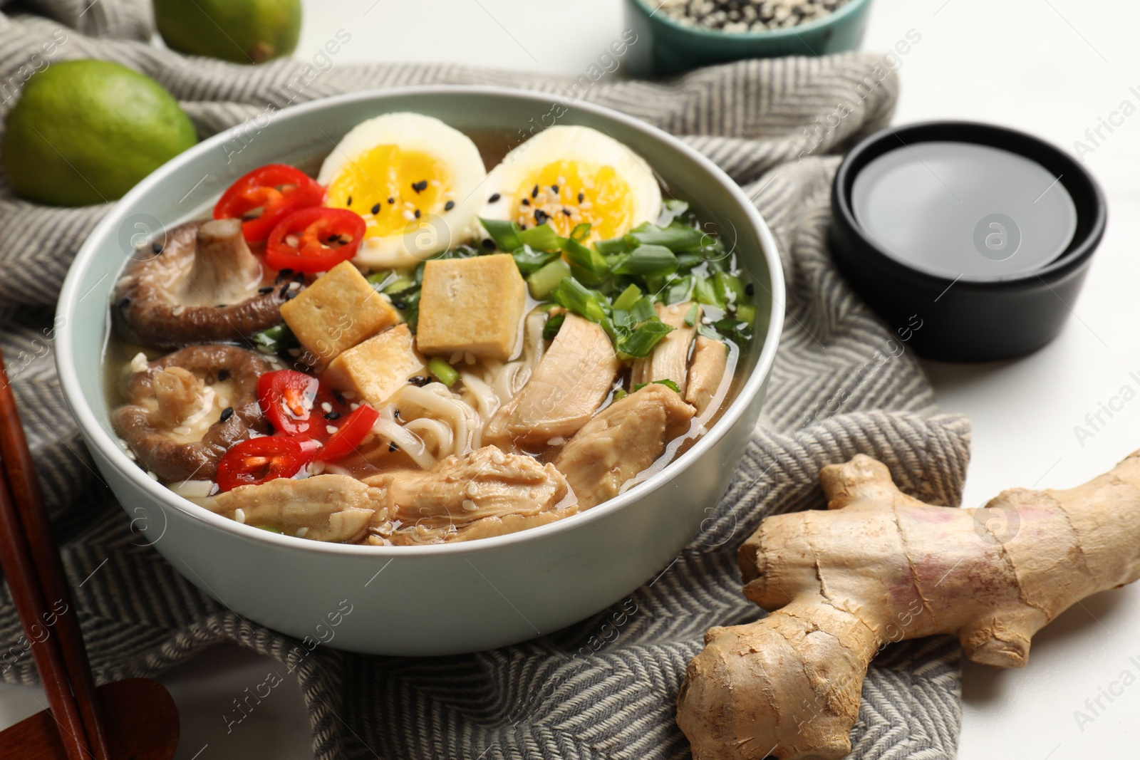 Photo of Bowl of delicious ramen, ingredients and chopsticks on white table, closeup. Noodle soup