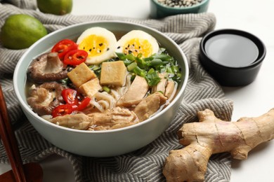 Bowl of delicious ramen, ingredients and chopsticks on white table, closeup. Noodle soup