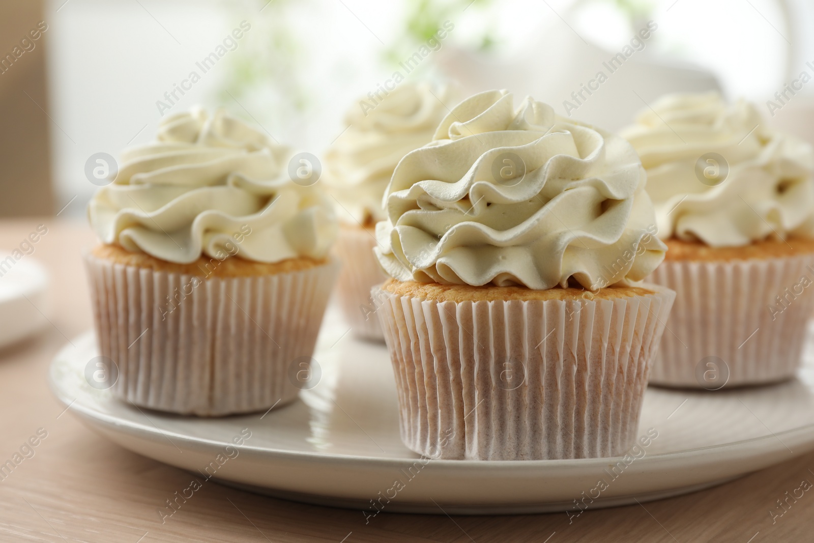 Photo of Tasty cupcakes with vanilla cream on light wooden table, closeup