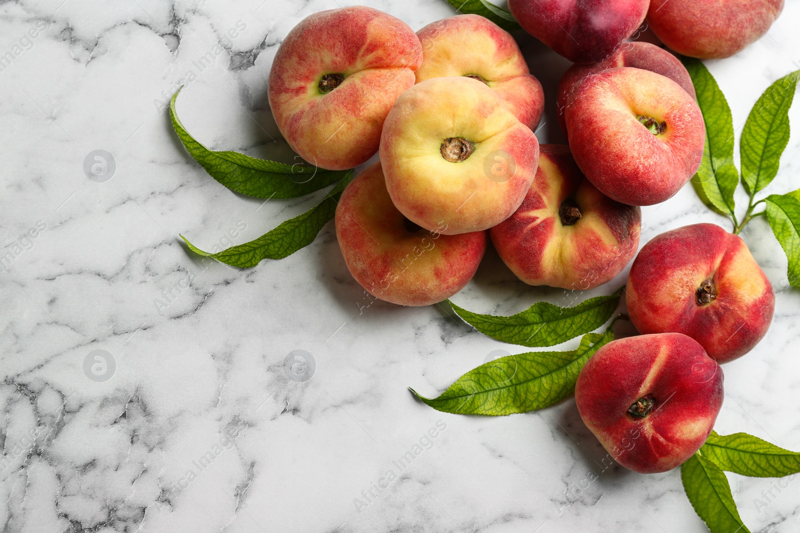 Photo of Fresh ripe donut peaches with leaves on white marble table, flat lay. Space for text