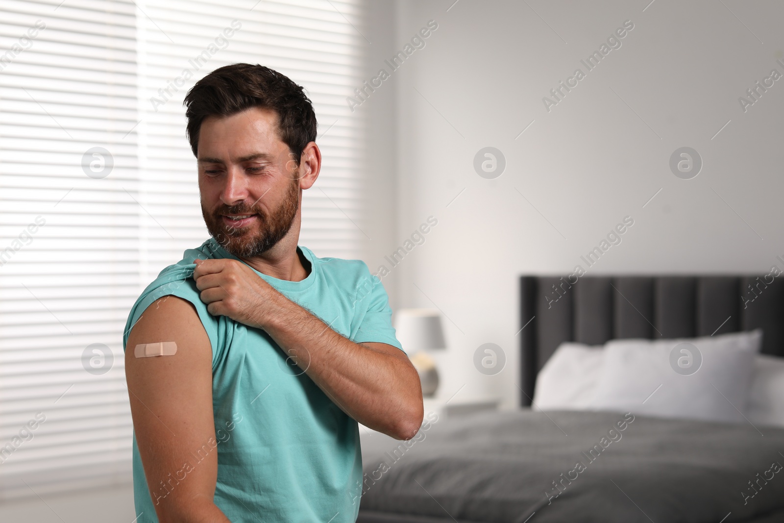 Photo of Man with sticking plaster on arm after vaccination in bedroom, space for text