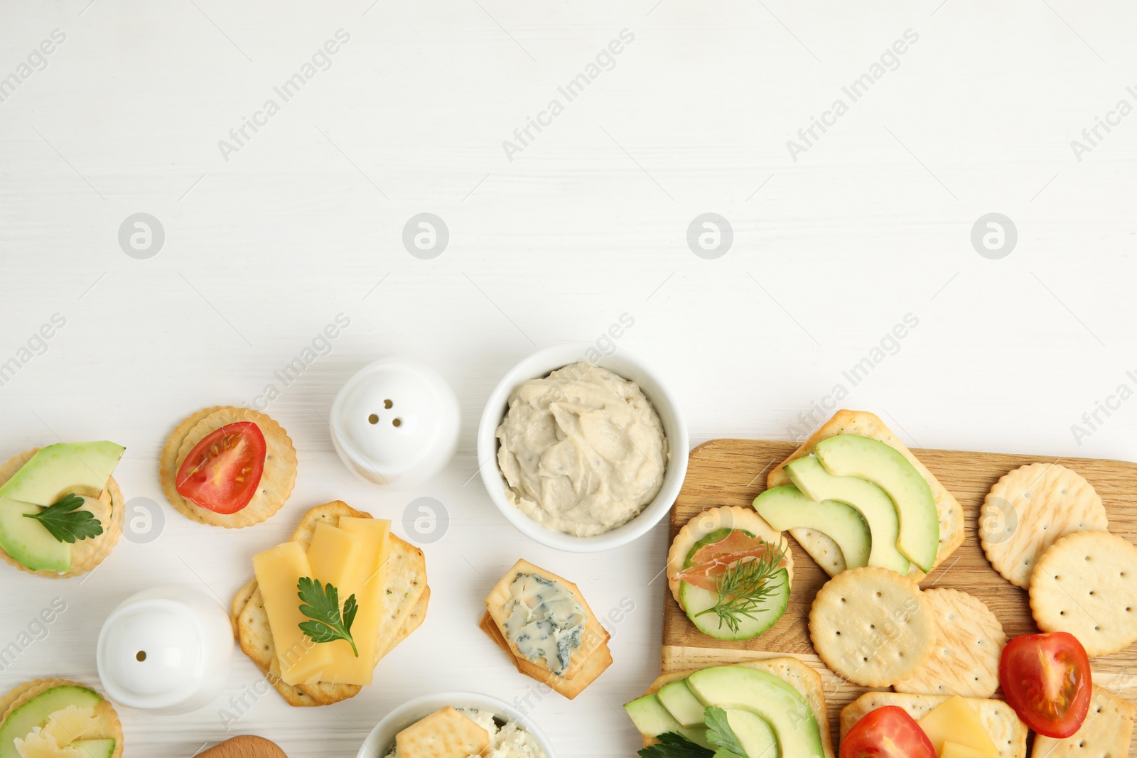 Photo of Different snacks with salted crackers on white wooden table, flat lay. Space for text