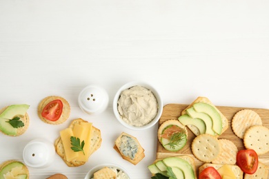 Different snacks with salted crackers on white wooden table, flat lay. Space for text