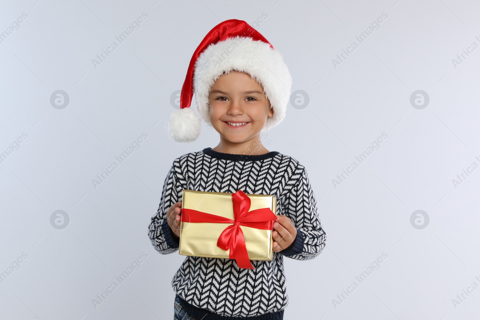 Photo of Happy little child in Santa hat with gift box on light grey background. Christmas celebration