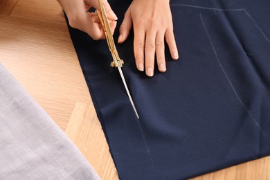 Photo of Woman cutting blue fabric with scissors at wooden table, closeup