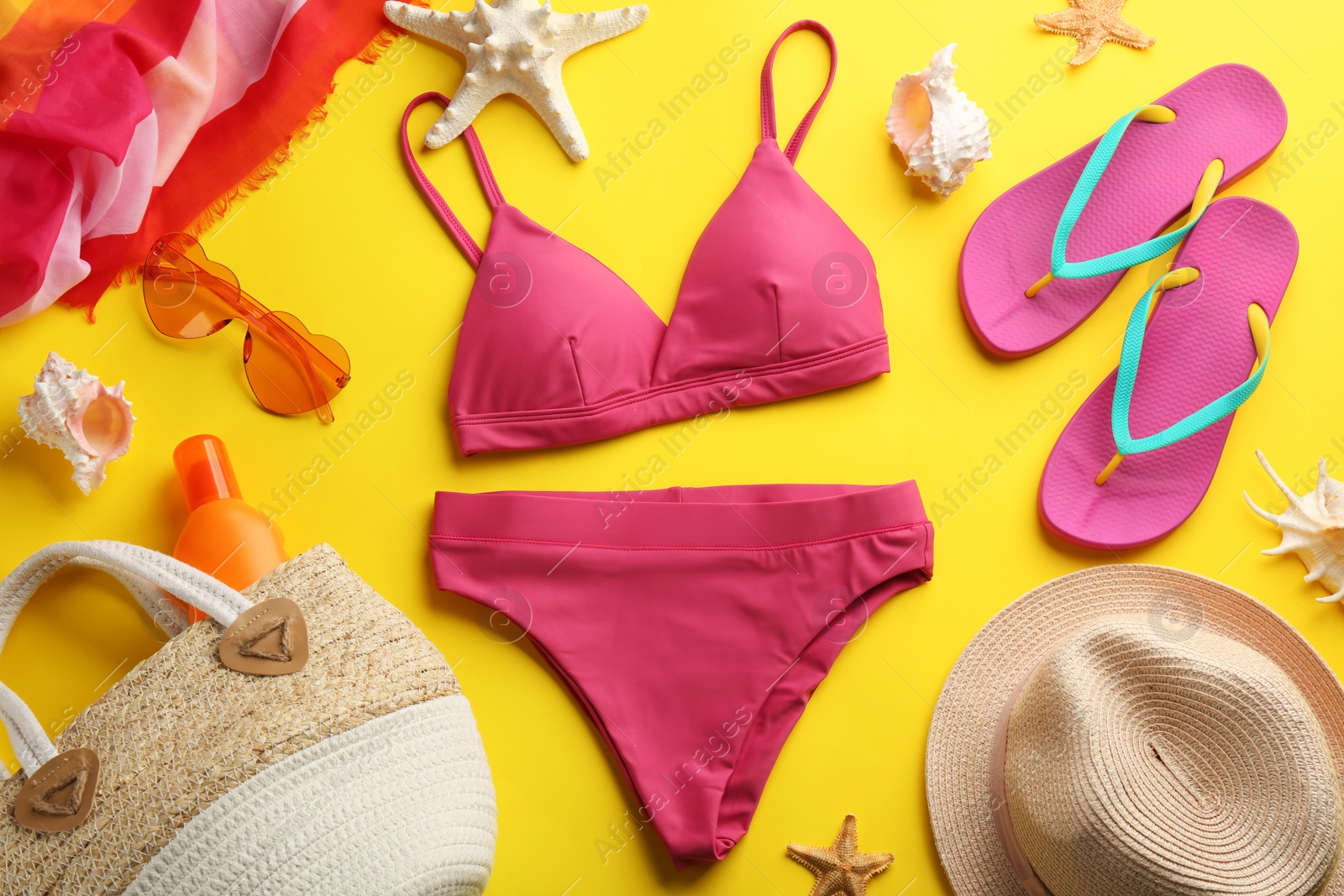 Photo of Beautiful pink bikini and beach accessories on yellow background, flat lay