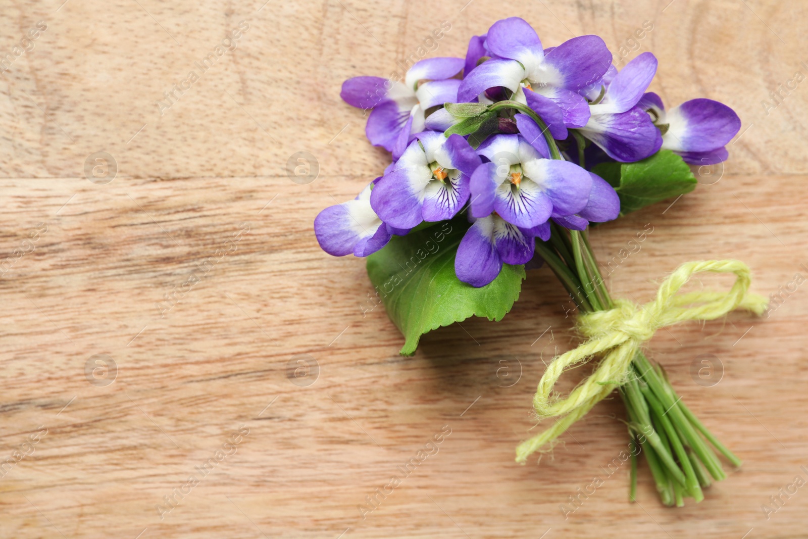 Photo of Beautiful wild violets and space for text on wooden table, top view. Spring flowers