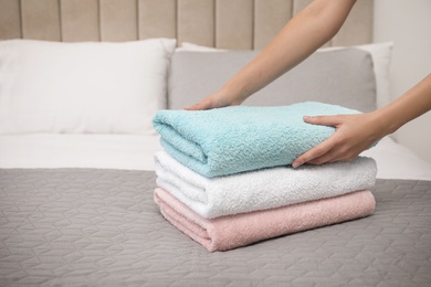 Photo of Woman folding soft clean terry towels on bed, closeup