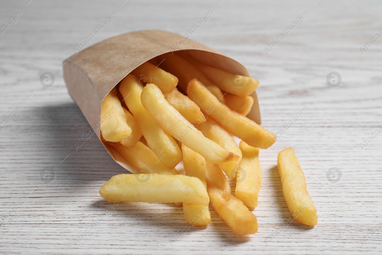 Photo of Delicious french fries in paper box on white wooden table, closeup