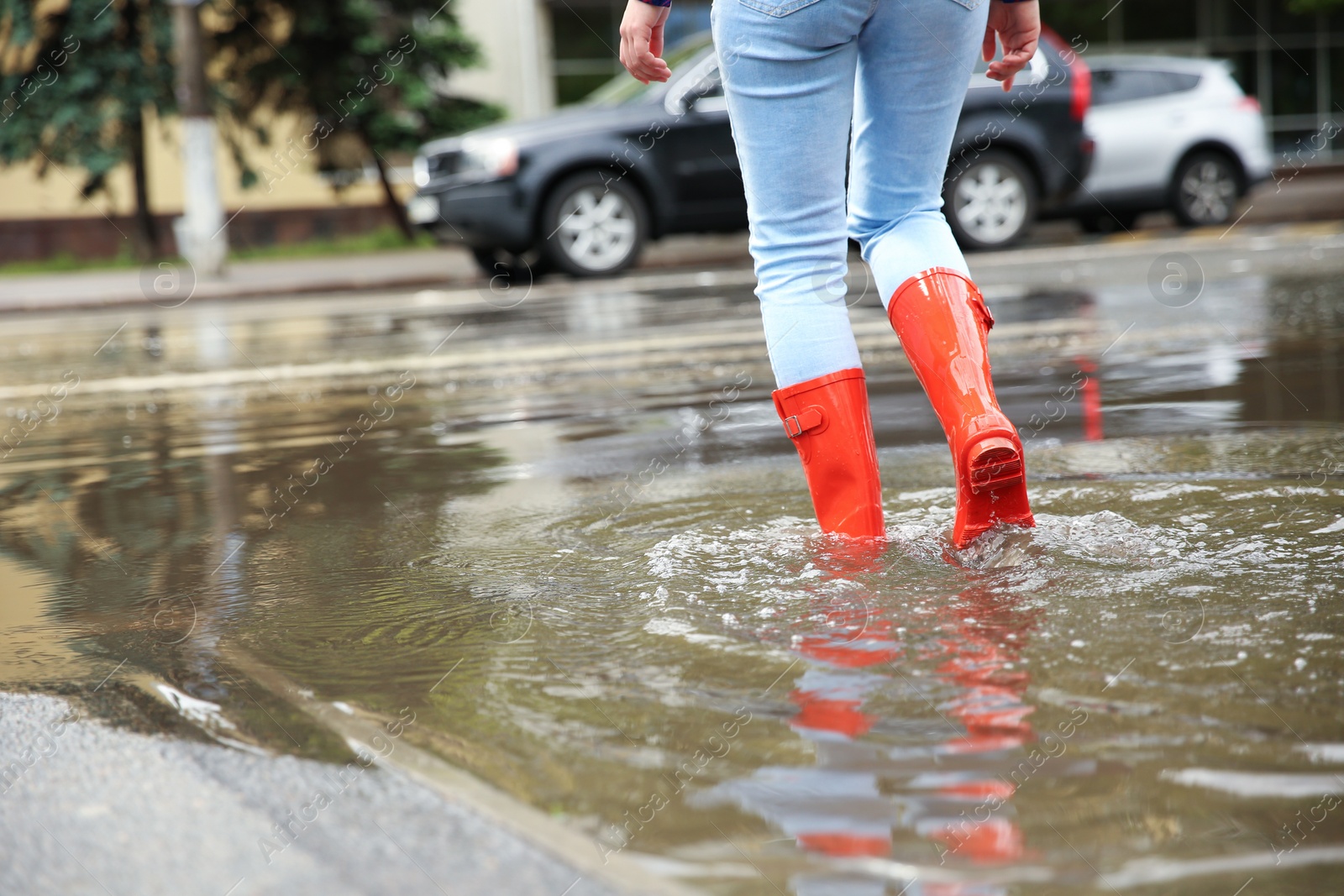 Photo of Woman with red rubber boots in puddle, closeup. Rainy weather