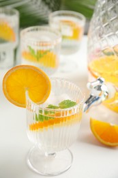 Delicious refreshing drink with orange and mint on white table