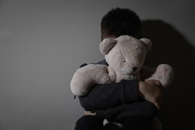 Scared little boy with teddy bear near beige wall, space for text. Domestic violence concept