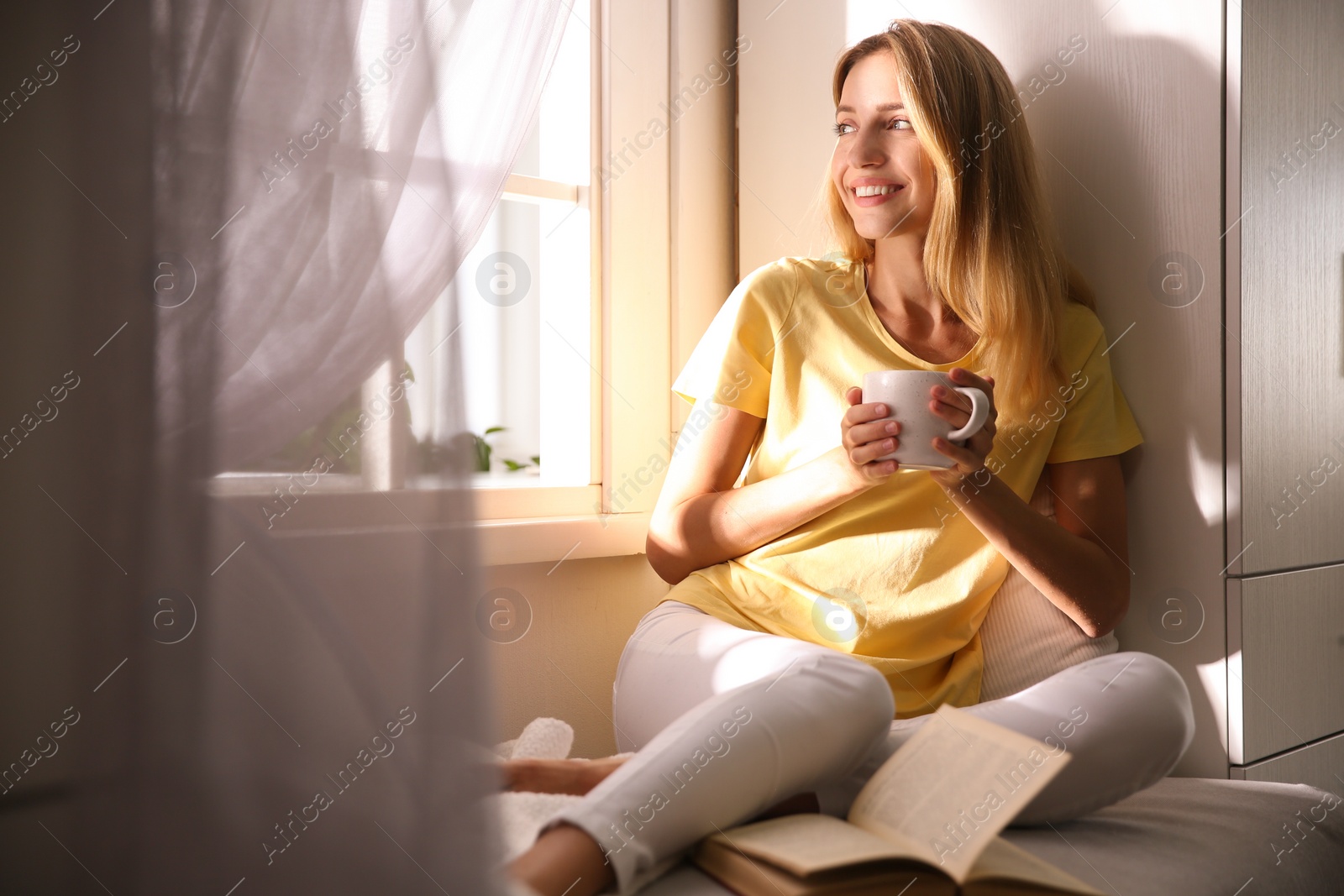 Photo of Beautiful young woman with cup of drink near window at home