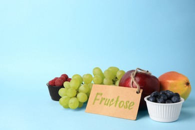 Photo of Card with word Fructose, delicious ripe fruits and berries on light blue background, space for text