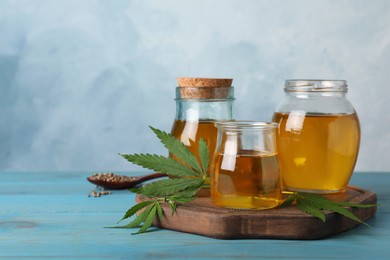 Photo of Hemp oil and leaves on light blue wooden table. Space for text