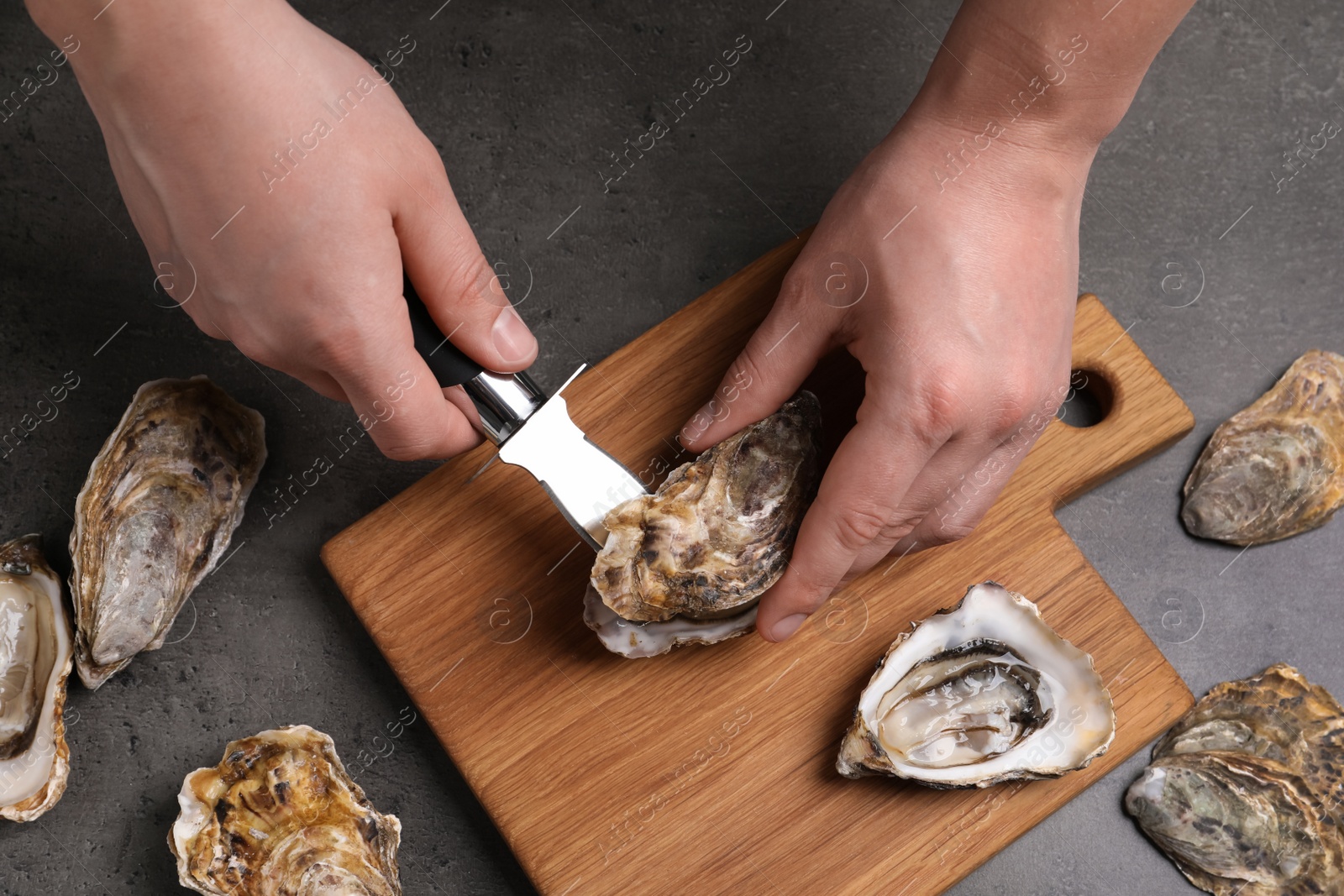 Photo of Man opening fresh oyster with knife at grey table, closeup