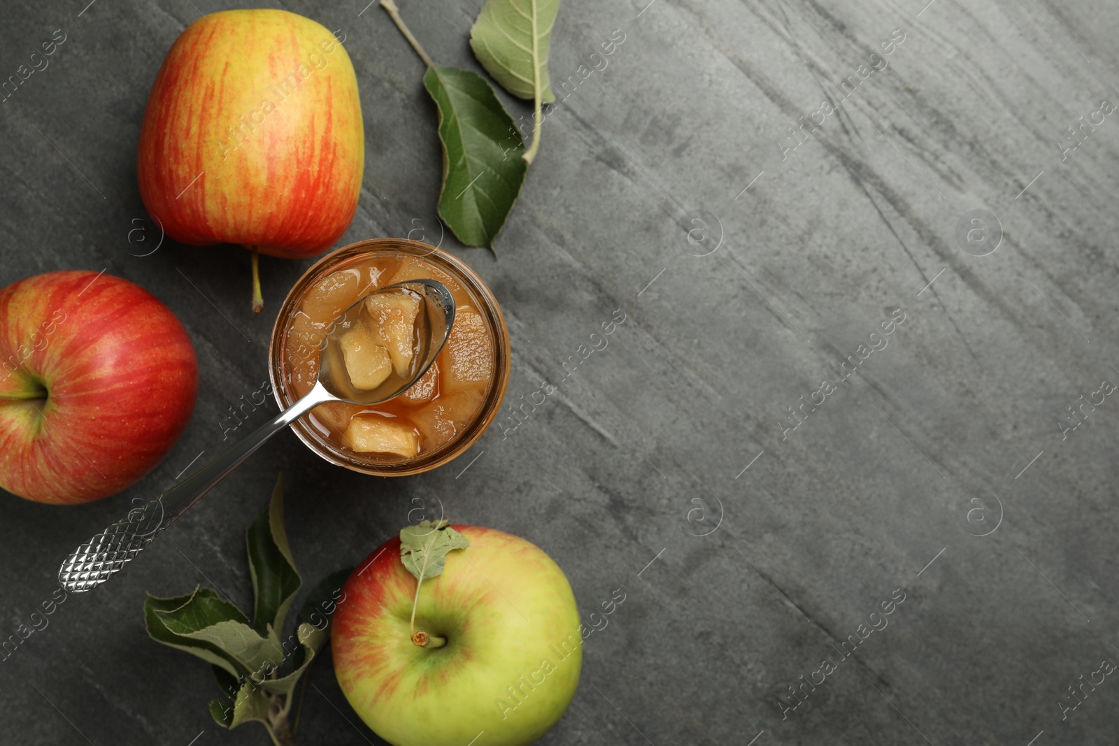 Photo of Tasty apple jam in glass jar and fresh fruits on grey table, flat lay. Space for text