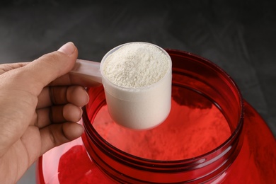 Woman holding measuring scoop of protein powder over jar, closeup
