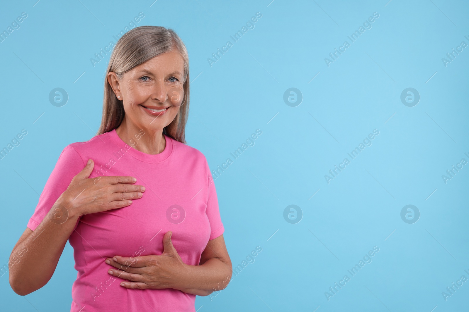 Photo of Beautiful senior woman doing breast self-examination on light blue background, space for text