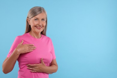 Photo of Beautiful senior woman doing breast self-examination on light blue background, space for text