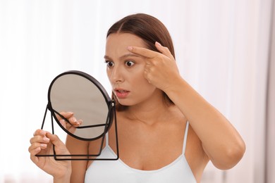 Woman with skin problem looking at mirror indoors