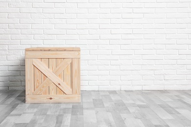 Photo of Wooden crate on floor at white brick wall. Space for text