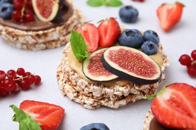 Photo of Tasty crispbreads with peanut butter, figs and berries on light table, closeup
