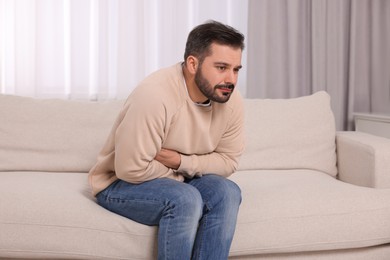 Photo of Man suffering from stomach pain on sofa at home