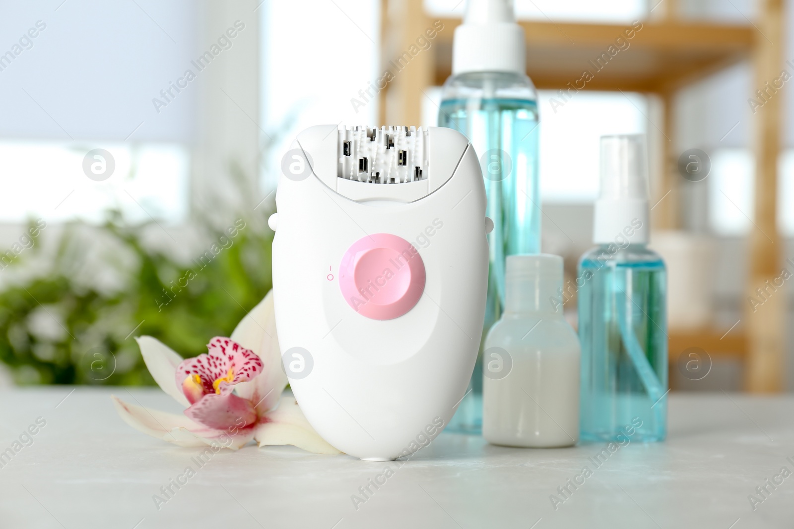 Photo of Modern epilator and beautiful flower on table