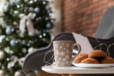 Book with treat on table and Christmas tree in stylish living room interior