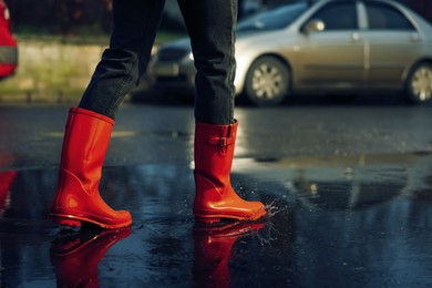 Photo of Woman with red rubber boots walking in puddle, closeup. Rainy weather
