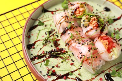 Photo of Delicious spring rolls with sauce and microgreens on yellow background, closeup