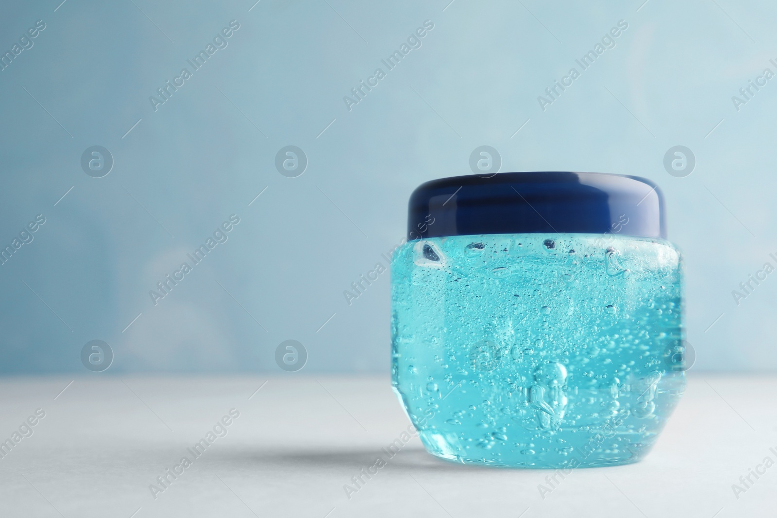 Photo of Jar of cosmetic gel on white table against light blue background, space for text