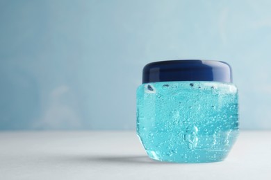 Photo of Jar of cosmetic gel on white table against light blue background, space for text