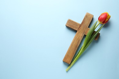 Easter - celebration of Jesus resurrection. Wooden cross and tulip on light blue background, top view. Space for text