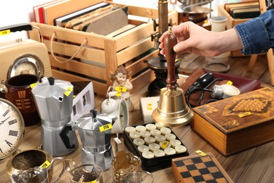 Photo of Woman holding bell near table with different stuff, closeup. Garage sale