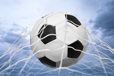Soccer ball in net against cloudy sky