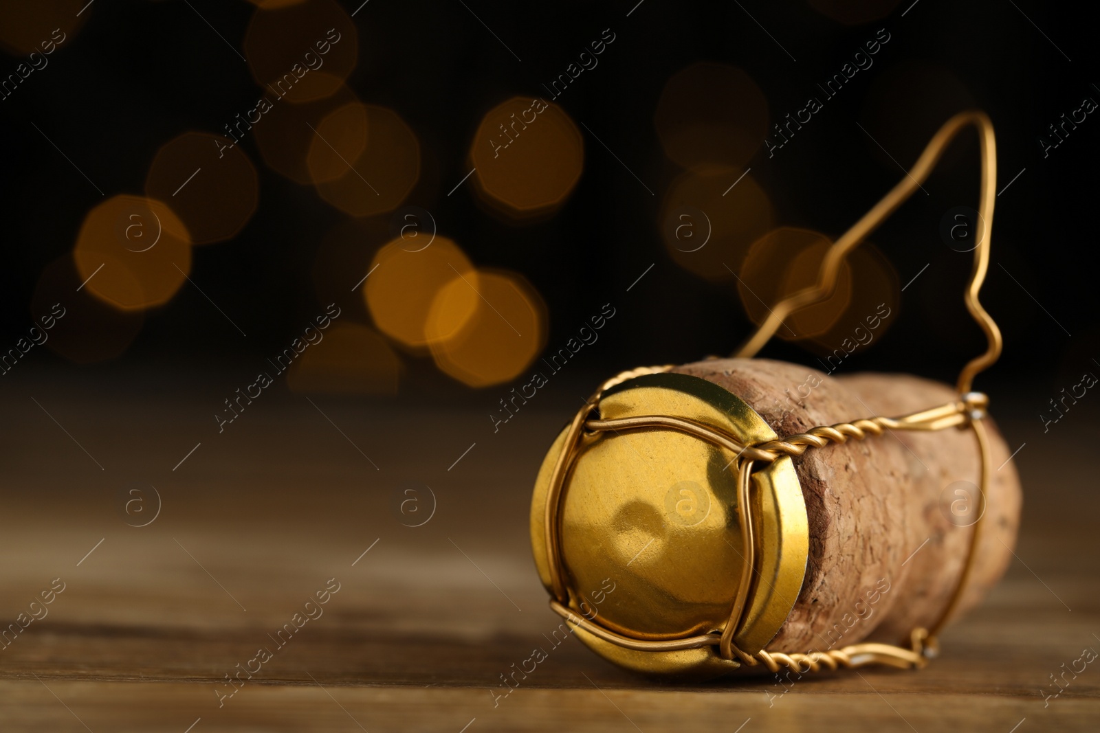 Photo of Closeup view of sparkling wine cork and muselet cap on wooden table against blurred festive lights, space for text. Bokeh effect