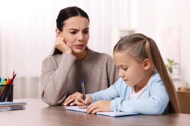 Photo of Dyslexia problem. Annoyed mother helping daughter with homework at table in room