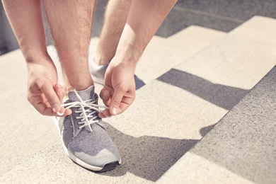 Photo of Young man tying shoelaces on his sneakers outdoors, closeup